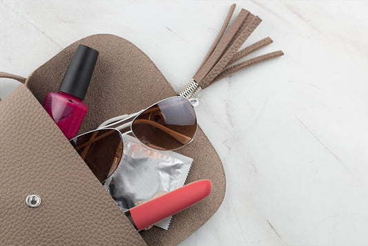 Open handbag with sunglasses, condom packet, nail polish, and red vibrator.