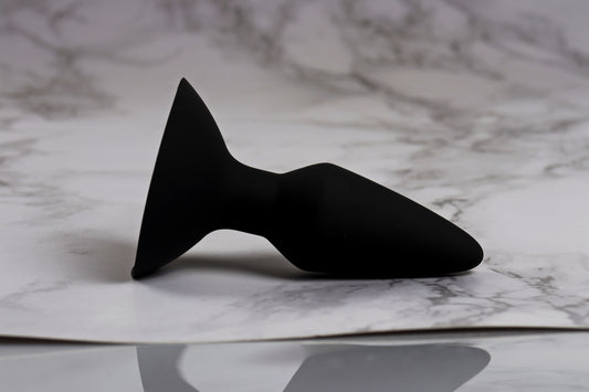 Black silicone butt plug standing on a white marble surface.