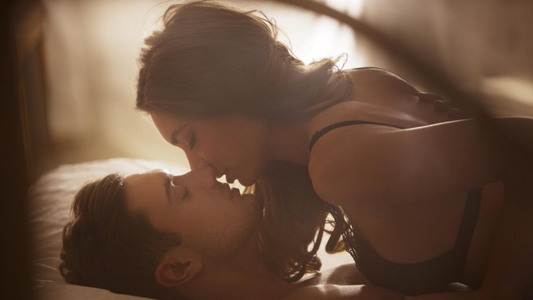 Couple leaning in for a kiss on a bed.
