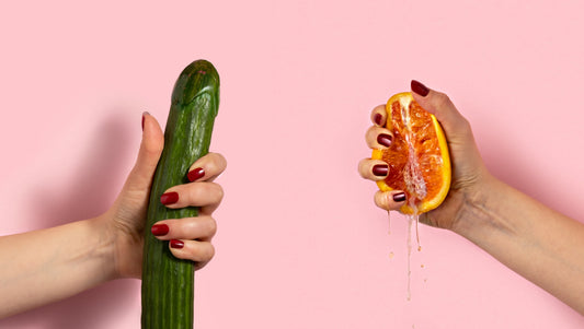 Hands holding a cucumber and grapefruit against a pink background.