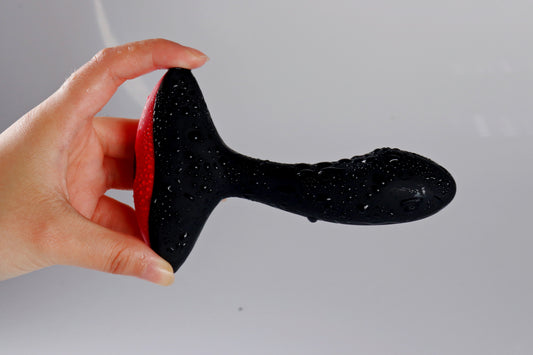 Hand holding a black and red prostate massager covered with water droplets.