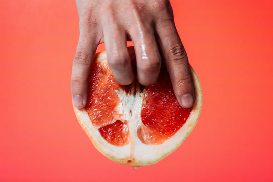 Hand pressing a halved grapefruit against a red background.
